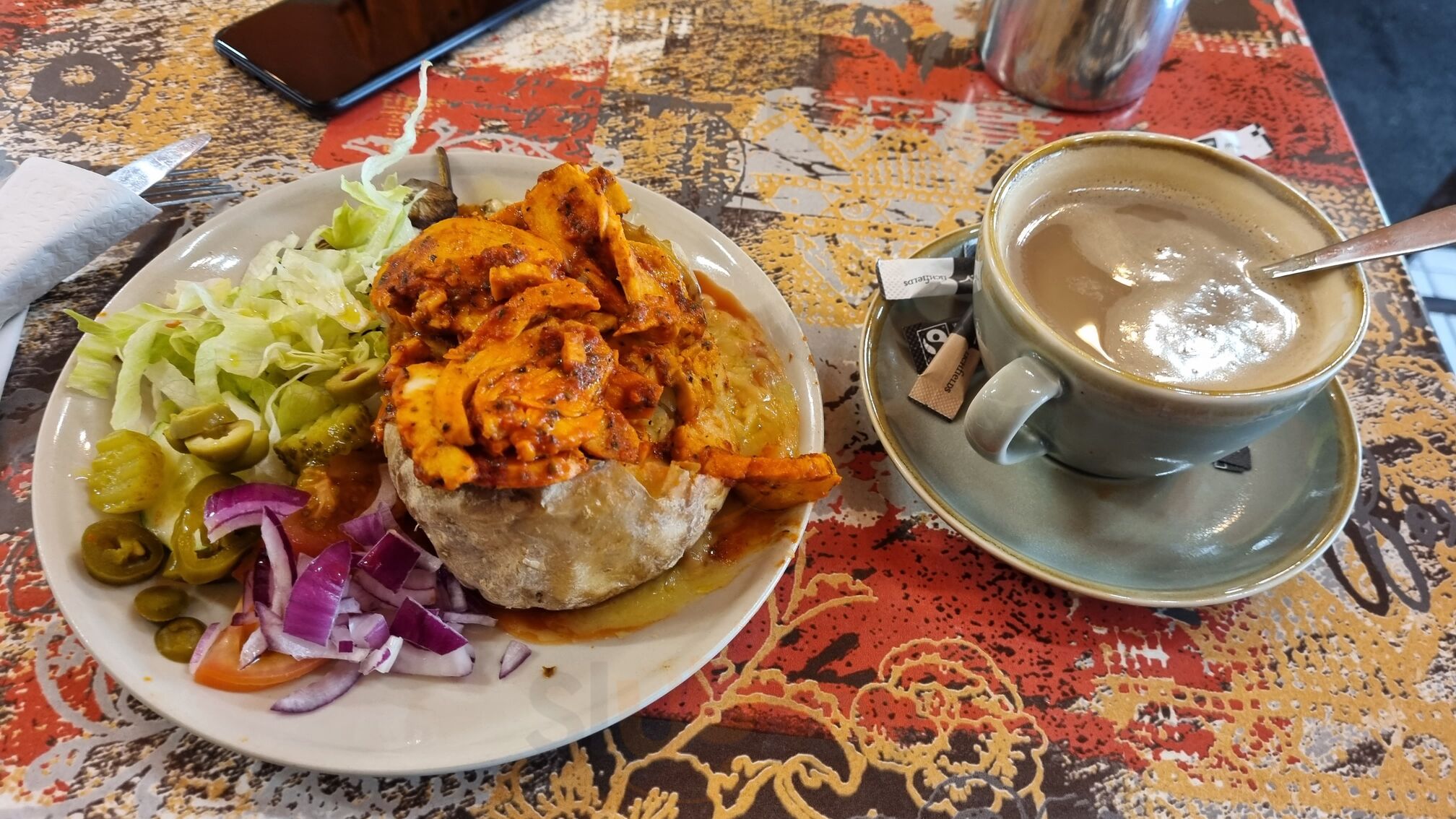 Milky coffee in a ceramic cup beside a jacket potato lunch at La Cigale